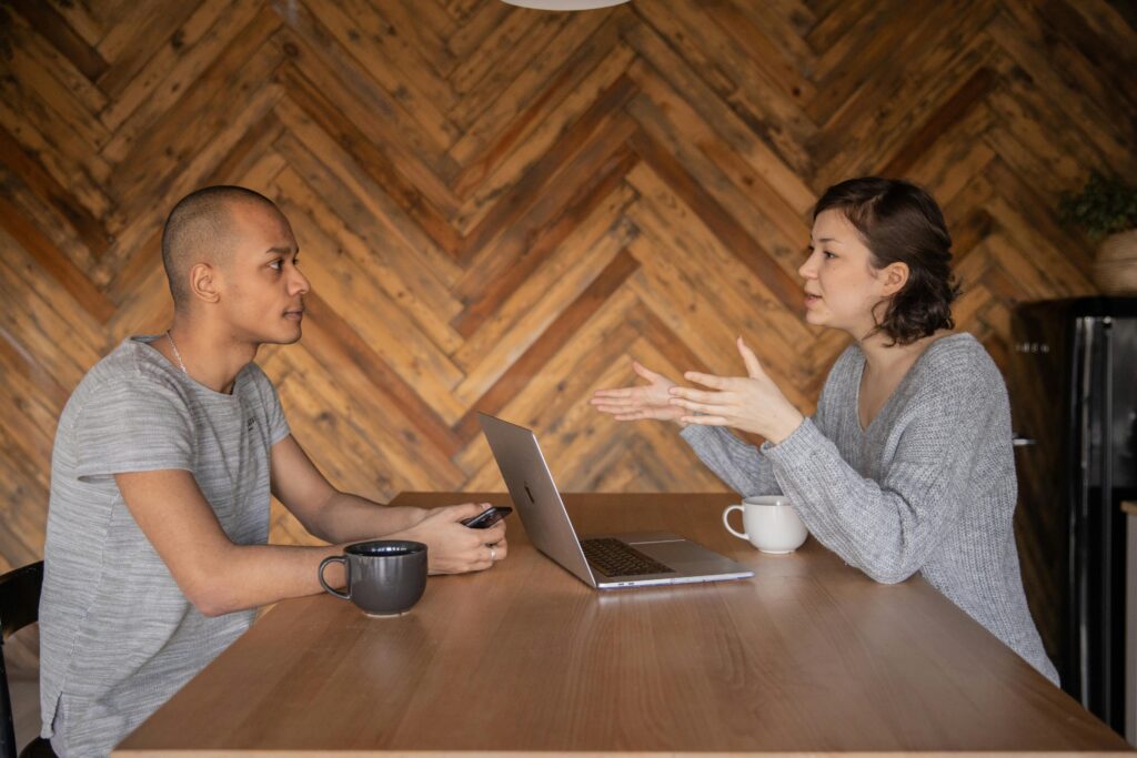 pexels photo 4049960 4049960 Focused woman explaining opinion to ethnic male coworker during business teamwork sitting at table with laptop and coffee cups in cozy kitchen against wooden wall and looking at each other