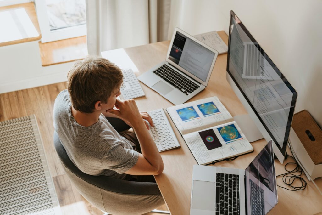 pexels photo 4974922 4974922 Top view of young programmer working on multiple laptops in a modern office setting.